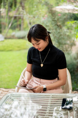 An attractive Asian woman sits at an outdoor table in a garden or backyard using her digital tablet.