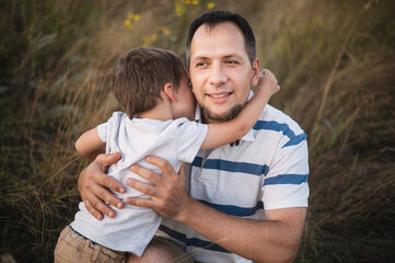 Father and son hug in front of a field. A happy dad hugs his little son against the backdrop of the sunset. Father's day holiday	
