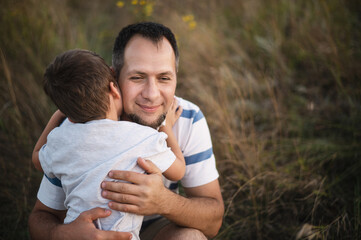Father and son hug in front of a field. A happy dad hugs his little son against the backdrop of the sunset. Father's day holiday	