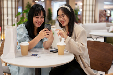 Two Asian female friends are enjoying talking while sitting together in a cafe in the shopping mall.