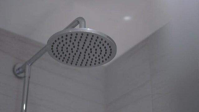 Chrome shower head turns on, water flows. Close up static shot.