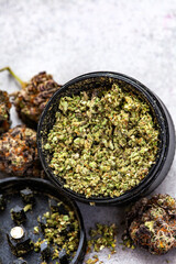 Black weed grinder with scattered buds of a purple indica strain. Selective focus, on light grey with copy space.

