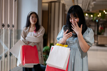 Young woman looks at her phone, smiling and covering her mouth with her hand, holding shopping bags