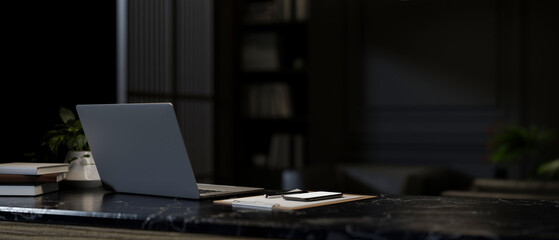 A close-up image of a laptop computer on a dark marble desk in a modern dark office.