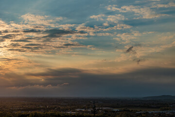 Obraz premium vista dettagliata del sole che tramonta all'orizzonte, dietro le nuvole scure di un temporale lontano e colora di arancione il resto del cielo azzurro parzialmente nuvoloso, sopra il nord est Italia