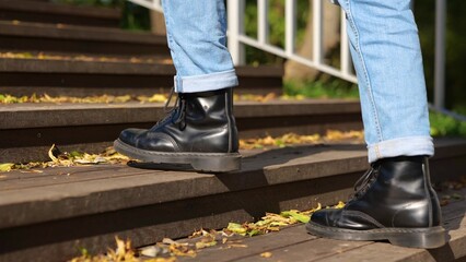 Guy in black boots going up the stairs in the park during sunny day. Leaves on the stairway....