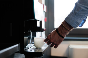 prendere o preparare un caffè in ufficio. mano sinistra di giovane uomo adulto mentre tiene in mano una piccola tazza bianca si prepara un caffè dalla macchinetta
