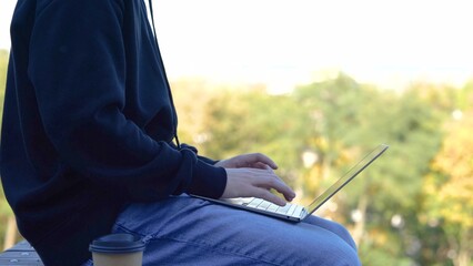 Young man typing on the laptop and working outdoor in the park. Side view. Copy space. Autumn season. Education, working concept. Slow motion - Powered by Adobe