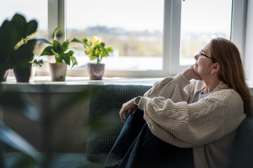 Caucasian attractive mature middle aged woman with glasses relaxing while sitting on sofa at home