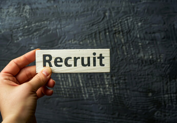 Hand holding Recruit with white wooden letters on a black background.
