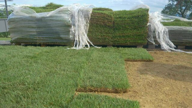 CLOSE UP: Unpacked patches of artificial grass lie stacked next to a scenic bare backyard. Plastic foil hangs off of two stacks of artificial grass getting installed in the backyard of a modern house.