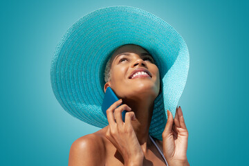 Happy woman portrait wearing blue sun hat and using mobile phone, isolated on turquoise bright...