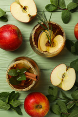 Glasses with apple cider, mint leaves and red apples on green wooden background, top view
