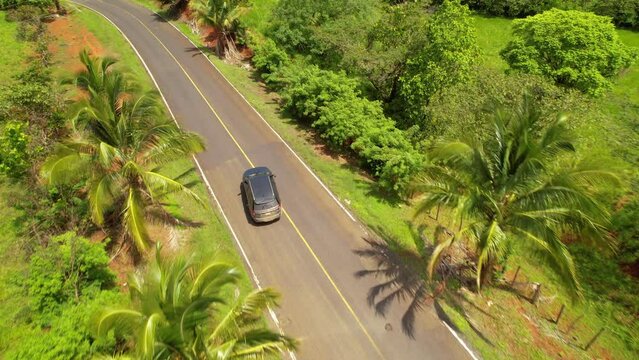 AERIAL: Following SUV car avoiding big asphalt holes on a paved road in tropics