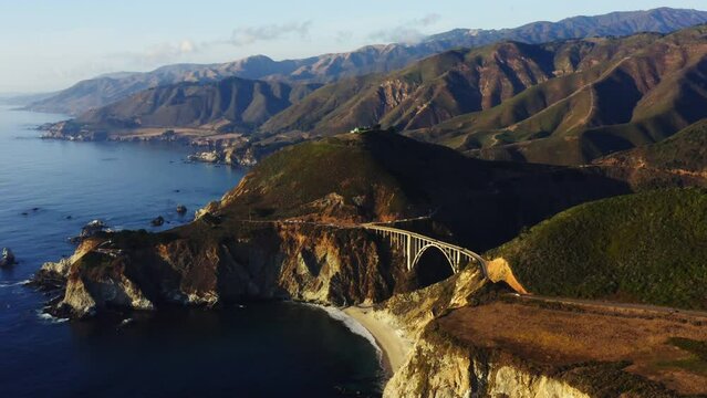 4k aerial footage of the Bixby Bridge in Big Sur Nature Park on coast of the Pacific Ocean on sun. One of the most beautiful roads in the USA. Colorful view of blue water and green hills of California
