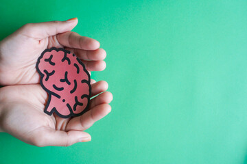 Woman hands holding human brain shape made from paper on light blue background. Awareness of...