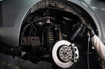 An auto mechanic applies anti-corrosion mastic to the underbody of a car.