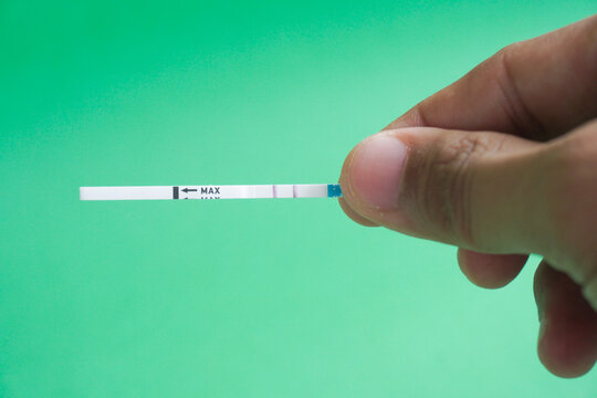 Pregnancy test pack hold by hand on top of green background.