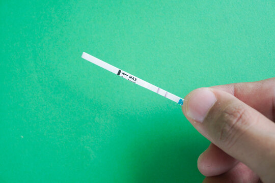 Pregnancy test pack hold by hand on top of green background.
