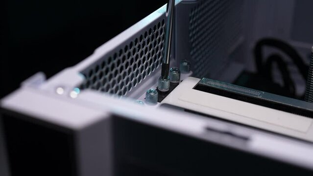 Closeup of technician hands unscrewing screws for remove graphic card from computer case. Close-up of master unscrews bolts with screwdriver. Concept of desktop PC maintenance and service, slow motion