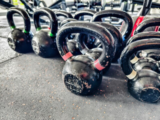 Multiple kettlebells of various weights lying idle on the rubber floor mat of the gym. Basic gym...