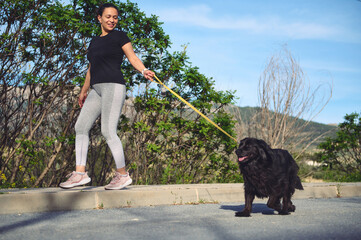 Happy female athlete, woman runner walking her dog on leash with performing morning jog on the...