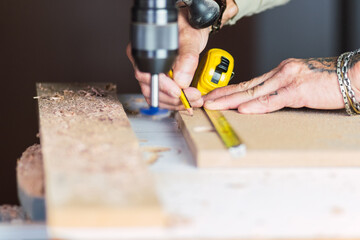 Carpenter holding a measure tape on the work bench. Woodwork and furniture making concept. Carpenter in the workshop marks out and assembles parts of the furniture cabinet