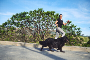 Full length portrait of young active woman running and walking her dog on leash on the nature...