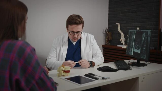 An experienced doctor, osteopath, conducts consultations in a modern clinic. A man consults a patient. The MRI image is open on the computer screen.