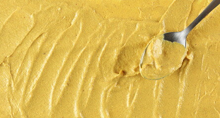 Yellow mustard sauce with metal spoon, spread background and texture, top view