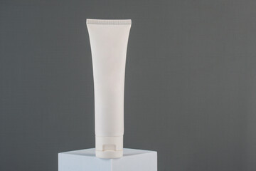 Plastic white tube for cream or lotion. Skin care or sunscreen cosmetic with stylish props on grey background.