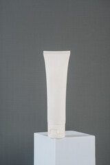 Plastic white tube for cream or lotion. Skin care or sunscreen cosmetic with stylish props on grey background.