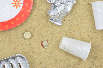 Beach after summer barbecue: plastic waste, aluminium grill tray, paper plate and so on. Top view.