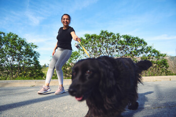 Happy woman walking her dog outdoors. Pretty female athlete dressed in gray leggings and black...