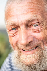 close-up portrait of happy senior man looking at camera. Park in background, Elderly mature people in outdoors leisure activity alone. One old male with beard and blue eyes look at you. Happiness