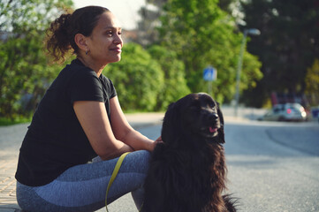 Side portrait of a beautiful young adult woman and her black cocker spaniel dog while walking it on...