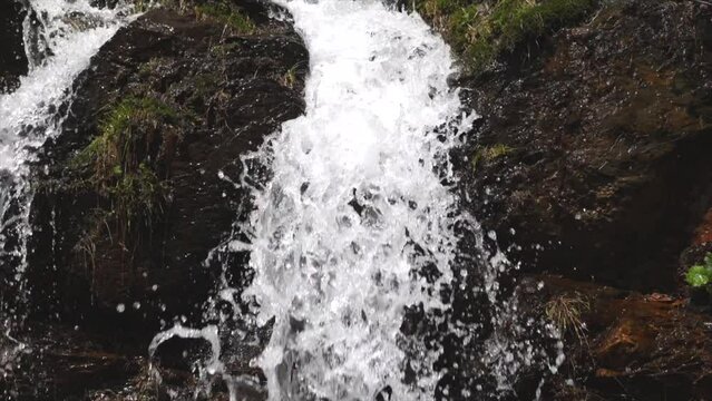 ripresa in tempo reale ed in primo piano di una piccola cascata in un ambiente naturale di montagna, illuminato dal sole, di giorno, in primavera