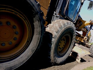 Photo from below of a car repairing the road. A yellow road service vehicle with a shovel and leveling the surface for laying fresh asphalt. The topic of road repair