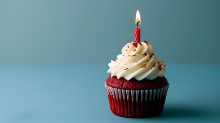 a birthday red velvet cupcake with birthday candle burning on a blue background