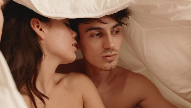 Romantic moment with a woman kissing a man on the cheek while they are cozily snuggled under a soft blanket together.