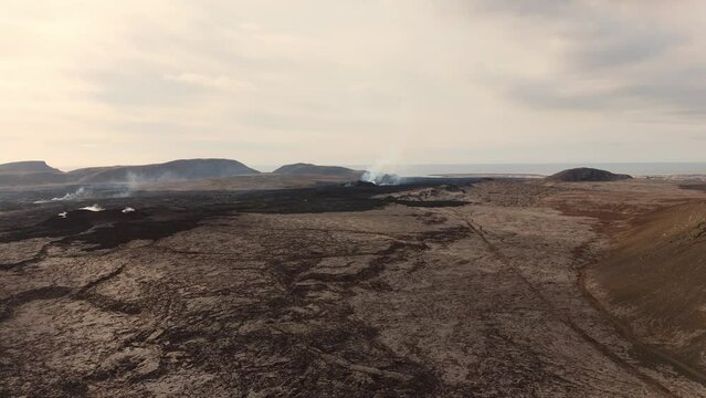 Desolate volcanic rock wasteland with smoking vents and volcano.