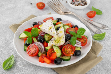 Greek salad of fresh juicy vegetables, feta cheese, herbs and olives on a white plate on a light concrete background. Healthy food. Copy space, top view.