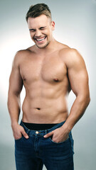 Fototapeta premium Shirtless man, laugh and muscles in studio with jeans for confidence, physical training or workout results on white background. Body, funny and model for bodybuilder abs, chest or transformation