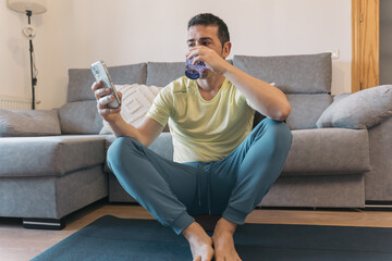 Man takes break from guided meditation on yoga block in living room, smiles while checking phone,...