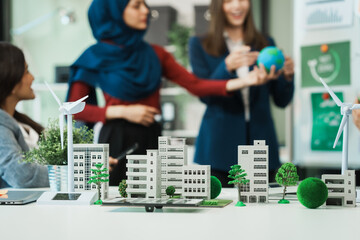 Diverse team, middle-aged Asian businessman, Caucasian young businesswoman, Muslim hijab-wearing businesswoman, meets in boardroom to discuss a wind turbine project for sustainable energy solutions.