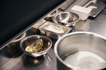 Table with cooking utensils, oyster and cream in bowls on kitchen in restaurant