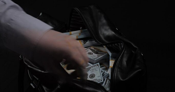 A business man was given a bribe of money dollars in a large bag on a black background. A businessman zips up a bag with a million dollars. Concept of bureaucracy, bribery.