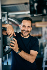 Portrait of a smiling male personal trainer, standing next to a squat rack, leaning on weights.