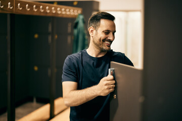 Smiling man, leaving his stuff in a gym locker room, preparing for training.