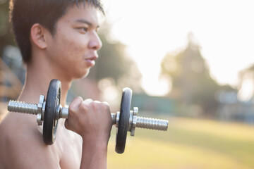 Asian preteen boy lifting dumbbells to loose weight and to do the bodybuild in grass field in late...